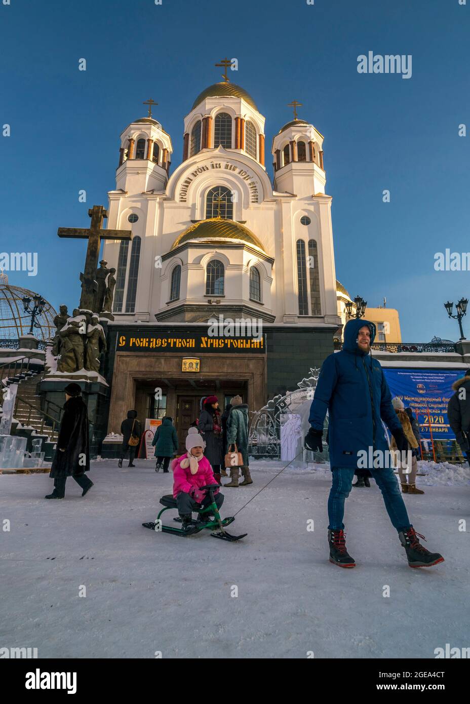 A father pulls his daughter on a sled in front of the Church of All Saints in Yekaterinburg in Russia. Stock Photo