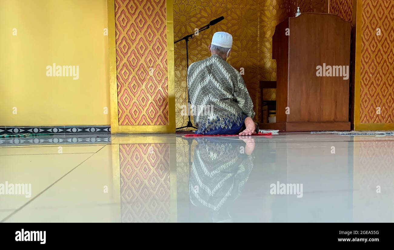 An old man wearing Batik praying in a mosque in Yogyakarta, Indonesia Stock Photo