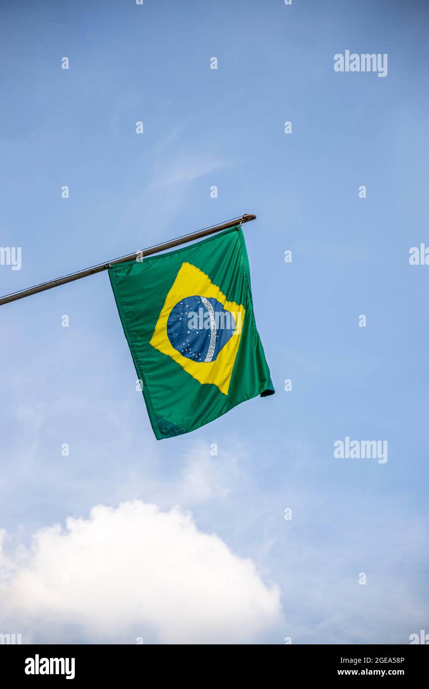 Brazilian flag displaying on a pole in front of the house against the blue sky. National flag of Brazil waving on a home hanging from a pole on a fron Stock Photo