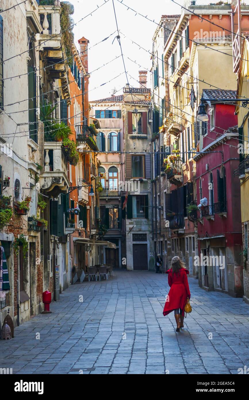 A woman in a red petticoat and beret strolls down the enchanting streets of Venice. Stock Photo
