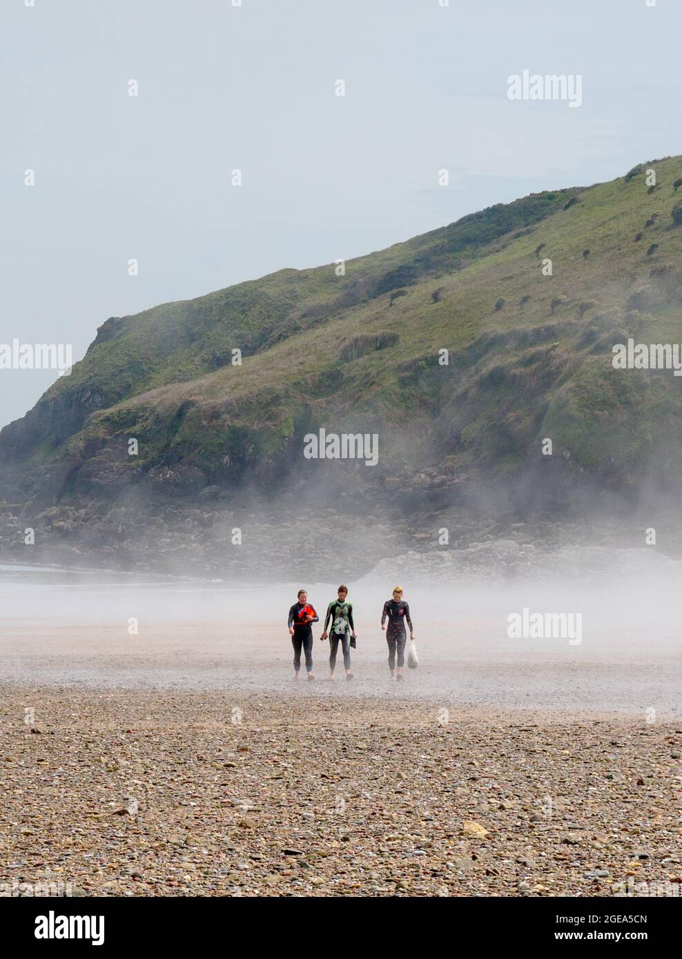 Three women surfers walking on beach at Freshwater East, Pembrokeshire, Wales Stock Photo