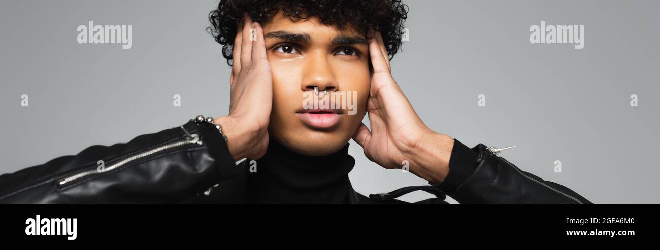 pierced african american man holding hands near face while looking away ...