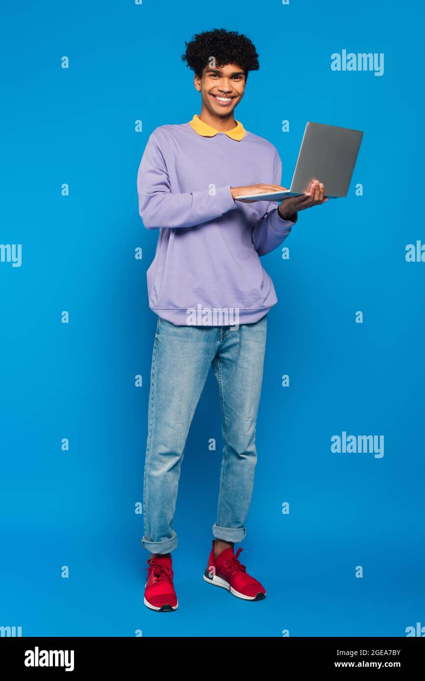 full length view of african american student using laptop on blue background Stock Photo