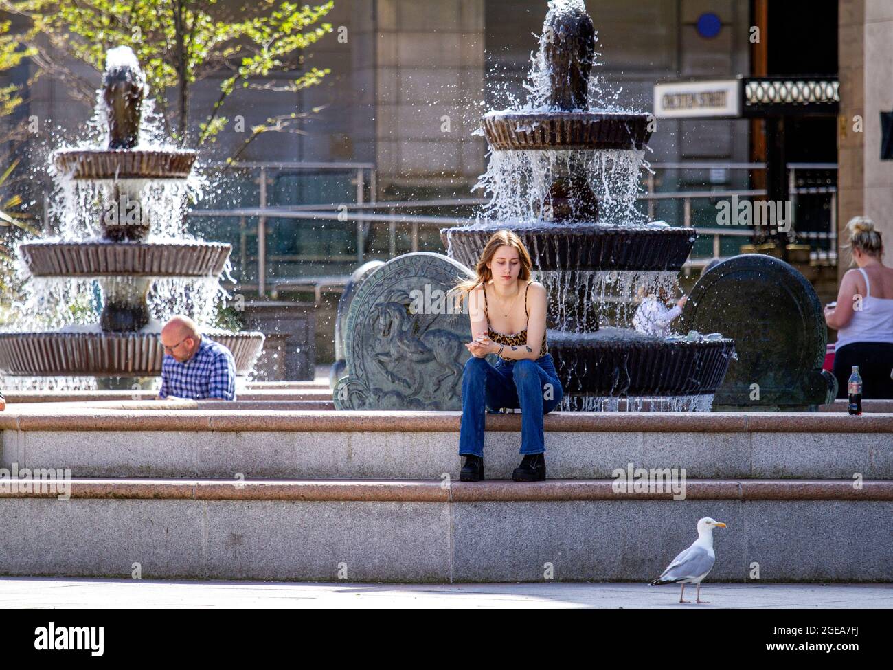 Dundee, Tayside, Scotland, UK. 18th Aug, 2021. UK Weather: Late Summer heatwave sweeping across North East Scotland with temperatures reaching 24°C. A glamorous young woman Annette Clarke sitting in the shade cooling off from the glorious hot sunny weather at the Caird Hall fountains in Dundee city centre. Credit: Dundee Photographics/Alamy Live News Stock Photo