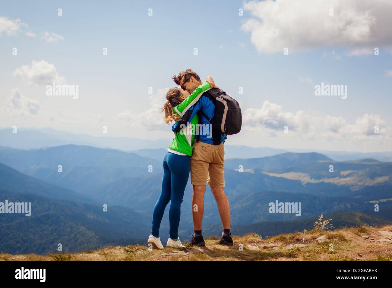 Happy couple of hikers honeymooners kissing on top of Hoverla mountain. Happy tourists travel in Carpathians. Tourism in summer Ukraine Stock Photo