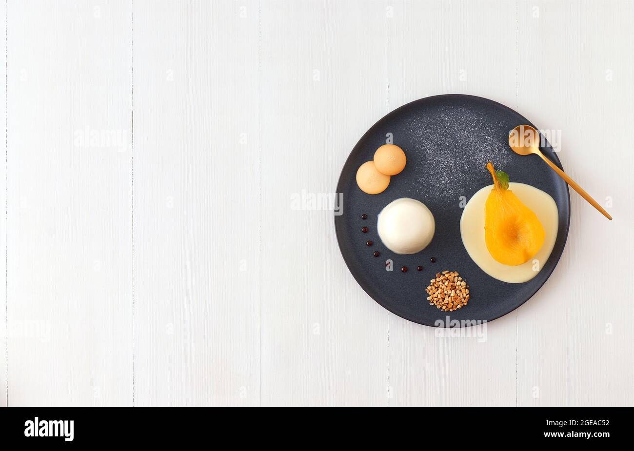 Panna cotta, traditional Italian dessert with muscat poached pears and creme Anglaise, crushed hazelnuts, caramel lentils and biscuits. High angle vie Stock Photo