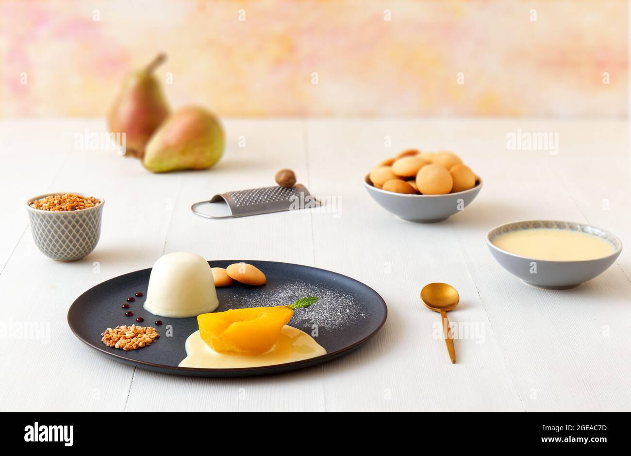Panna cotta, traditional Italian dessert with muscat poached pears and creme Anglaise, crushed hazelnuts, caramel lentils and biscuits. High angle vie Stock Photo