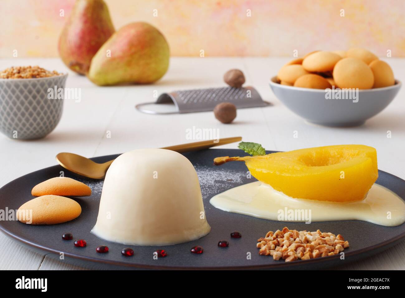 Panna cotta, traditional Italian dessert with muscat poached pears and creme Anglaise, crushed hazelnuts, caramel lentils and biscuits. High angle vie Stock Photo