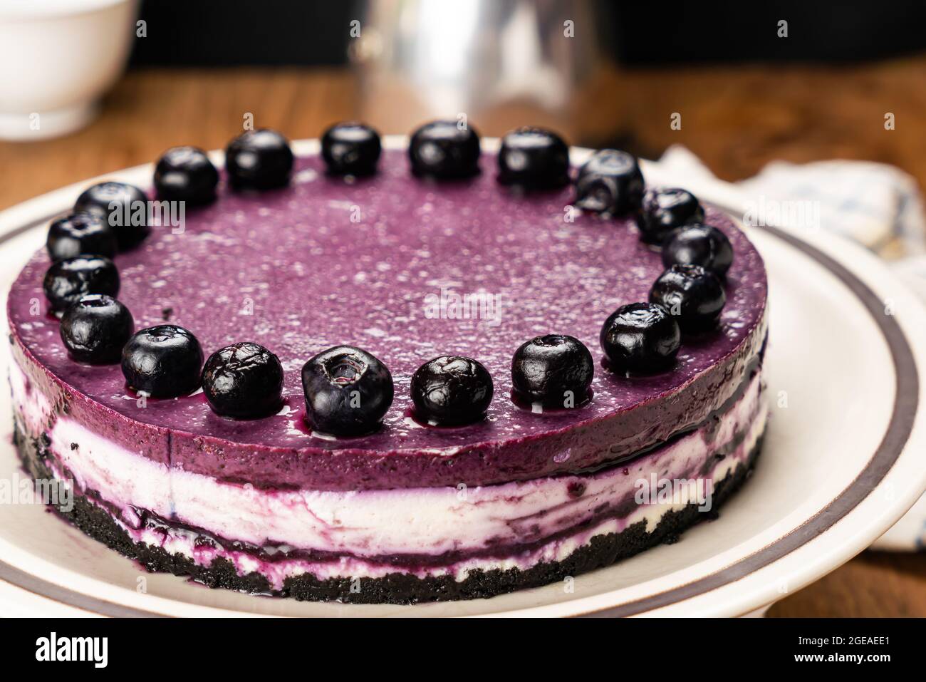 Closeup of delicious homemade blueberry cheesecake garnished with preserved blueberry in brown ceramic dish with table cloth, moka pot coffee maker, w Stock Photo