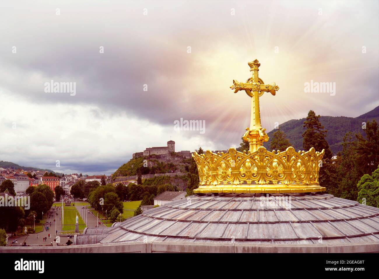 Golden crown and cross on the roof of the Basilica of the Virgen Mary in Lourdes France. The medieval castle in background. Stock Photo