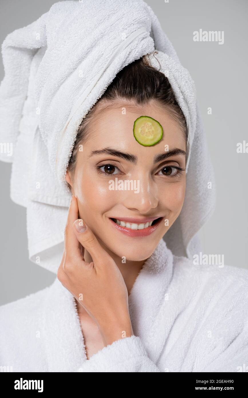happy young woman with towel on head and sliced cucumber on face isolated on grey Stock Photo