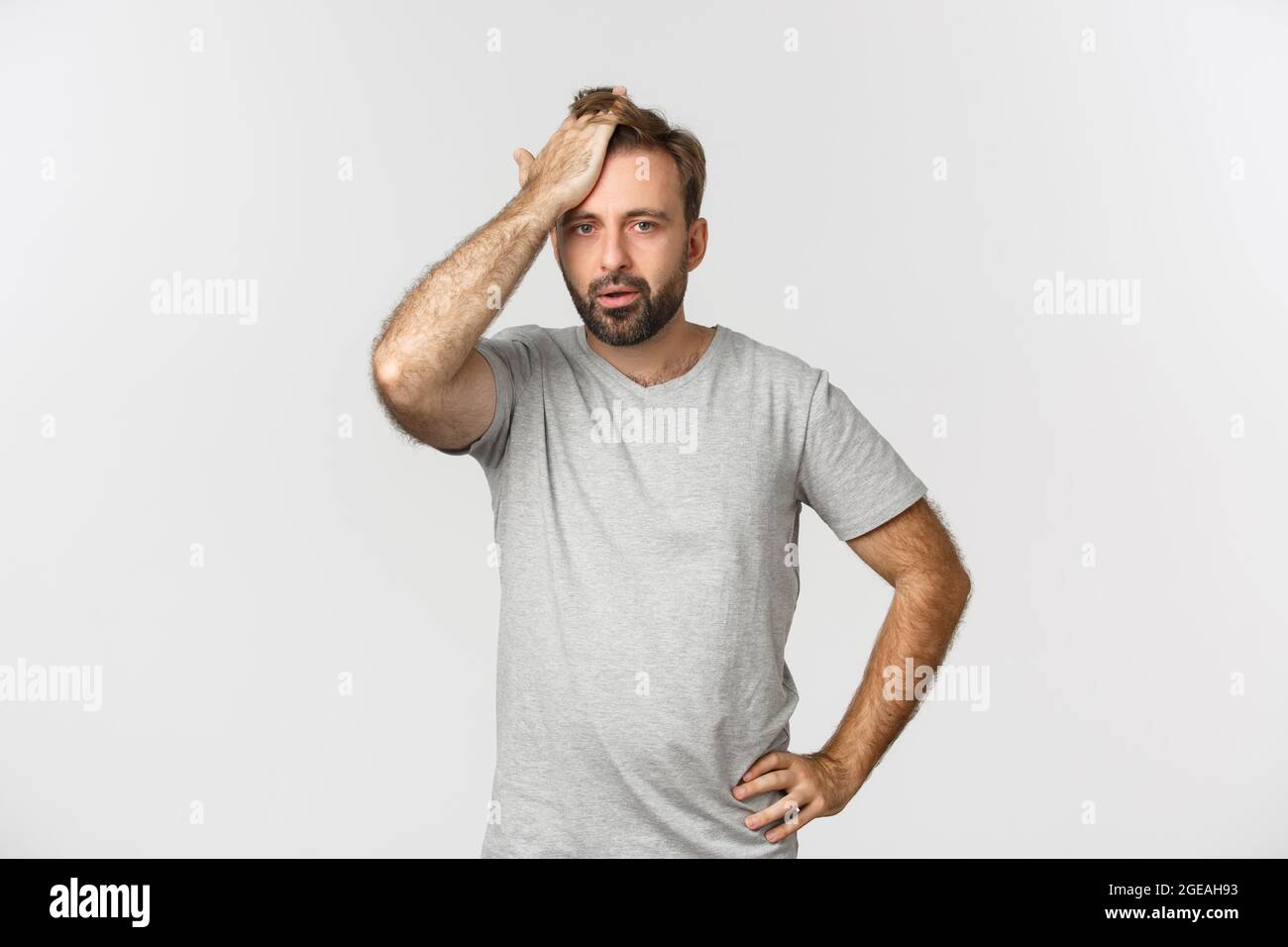 Troubled bearded man in gray t-shirt, slap forehead and sighing bothered by problem, standing over white background distressed Stock Photo