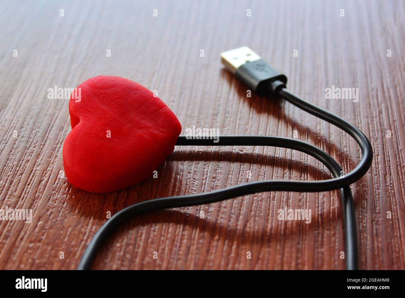 Red heart with usb cable on wooden background. Love and technology concept Stock Photo