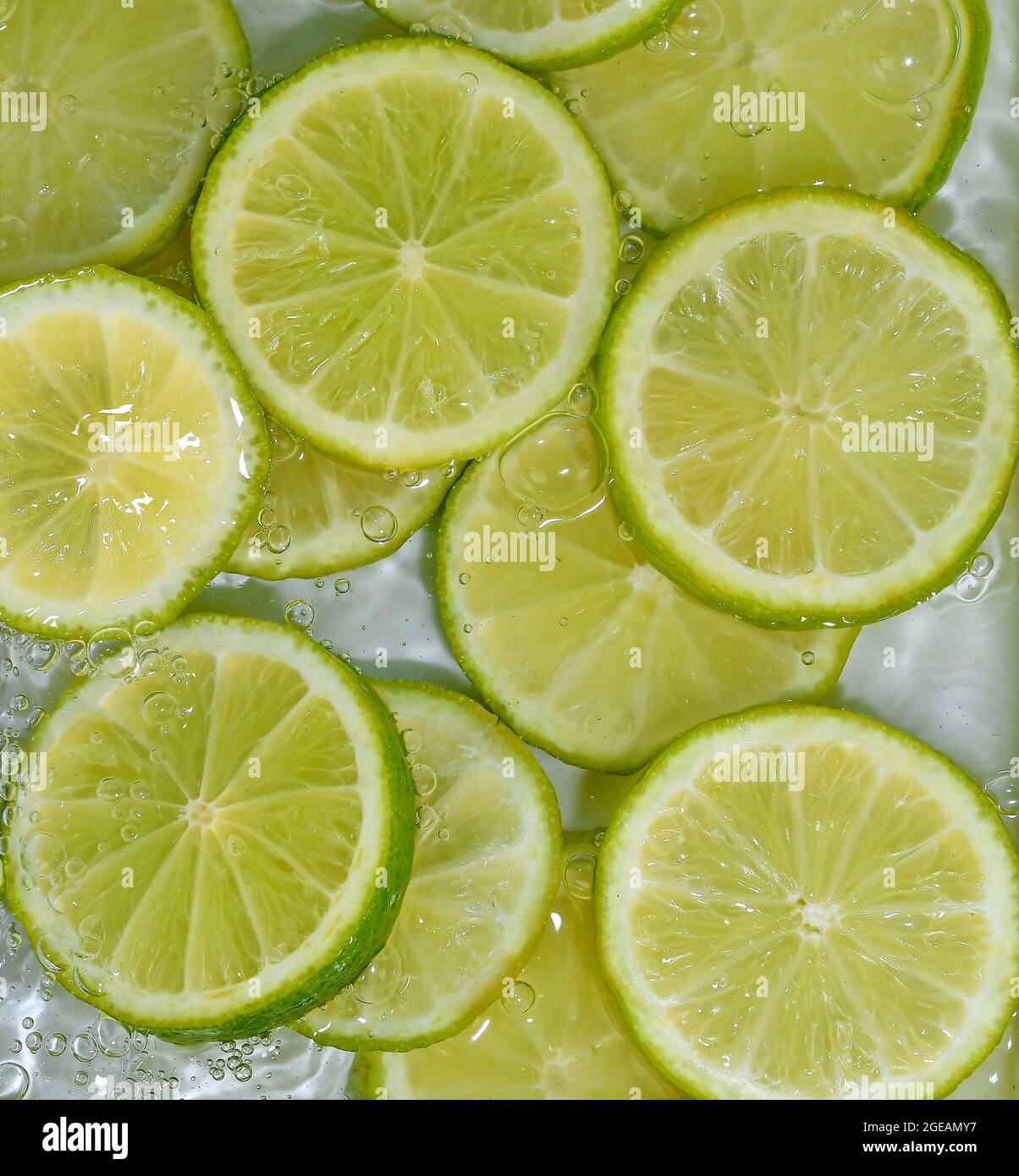 Close-up fresh slices of green limes on white background. Slices of limes in sparkling water on white background, closeup. Citrus soda Stock Photo