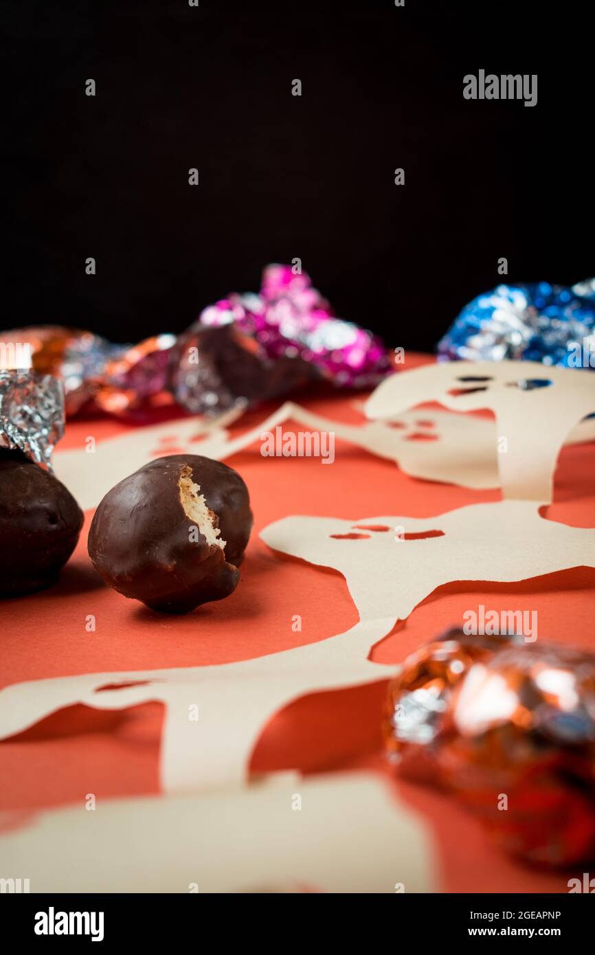 Some chocolates, different colorful wrappers and paper ghosts on orange surface Stock Photo