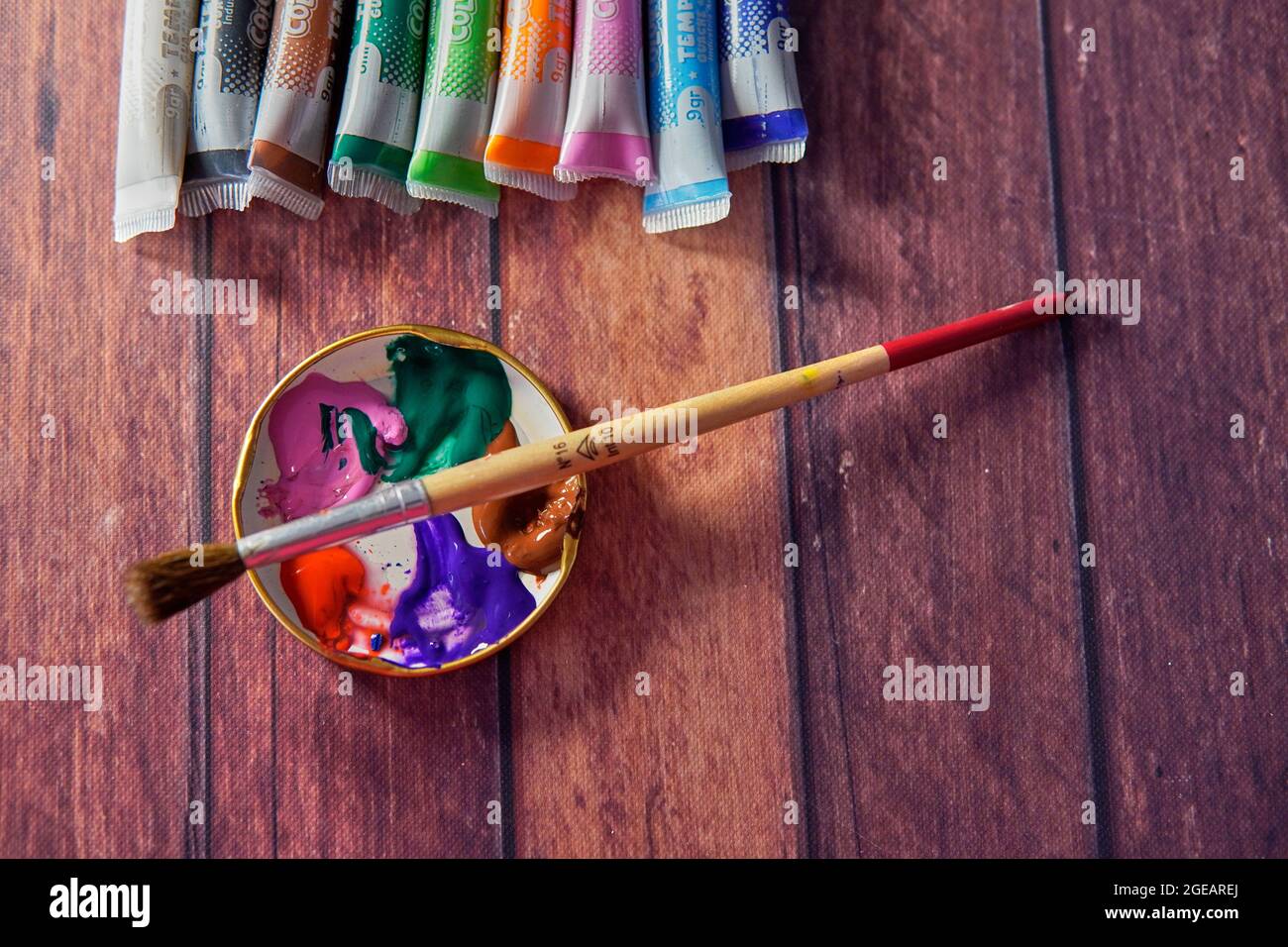 A collection of well used art paint brushes with a highly colourful  abstract artwork as a background Stock Photo - Alamy