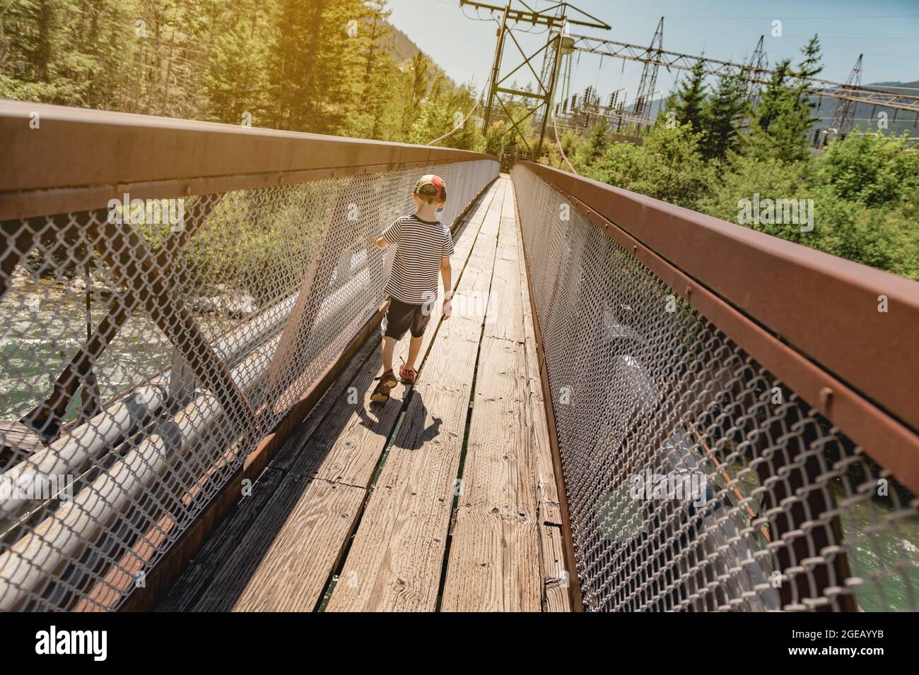 Young boy walking across a suspension bridge spanning the Skagit river in North Cascades National Park. Stock Photo