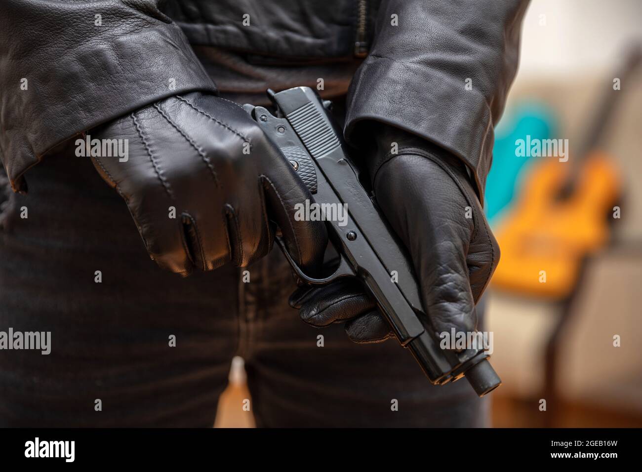 Gloved man arming his pistol. Killer wearing leather jacket holding a gun preparing to shoot, closeup view. Armed gunman, murderer concept Stock Photo