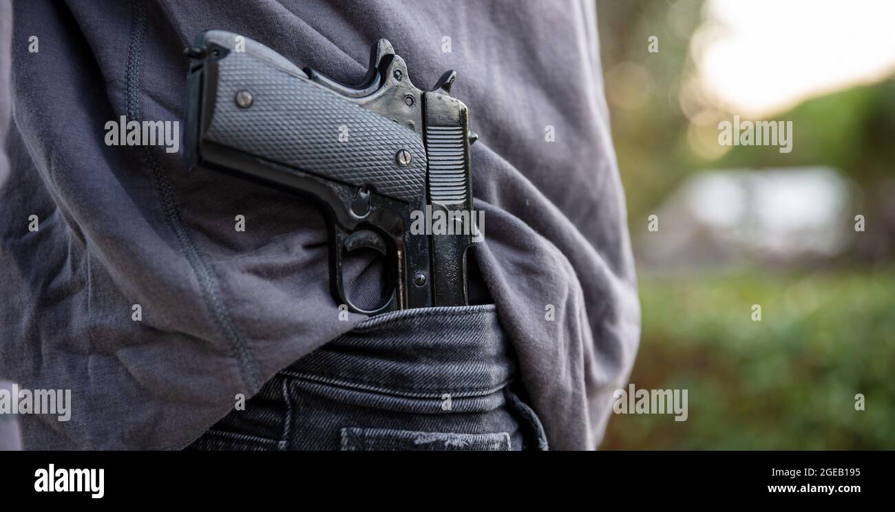Armed man carrying a pistol in his jeans waistband, blur outdoor nature background. Threat, violence and danger concept Stock Photo