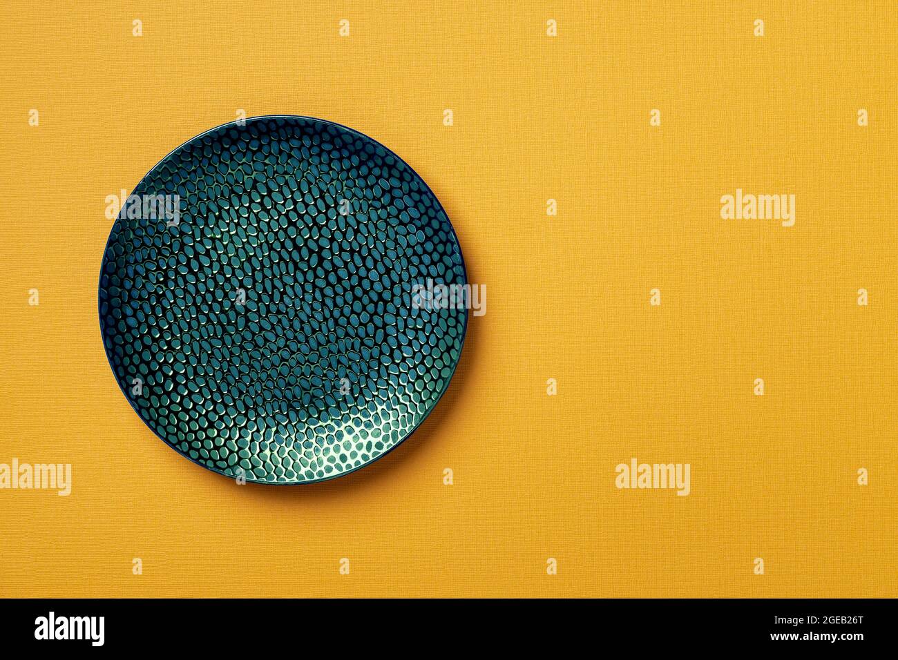 Textured turquoise teal round plate on a textured yellow background. Modern ceramic crockery and tableware for stylish food design. Empty dishes. Stock Photo