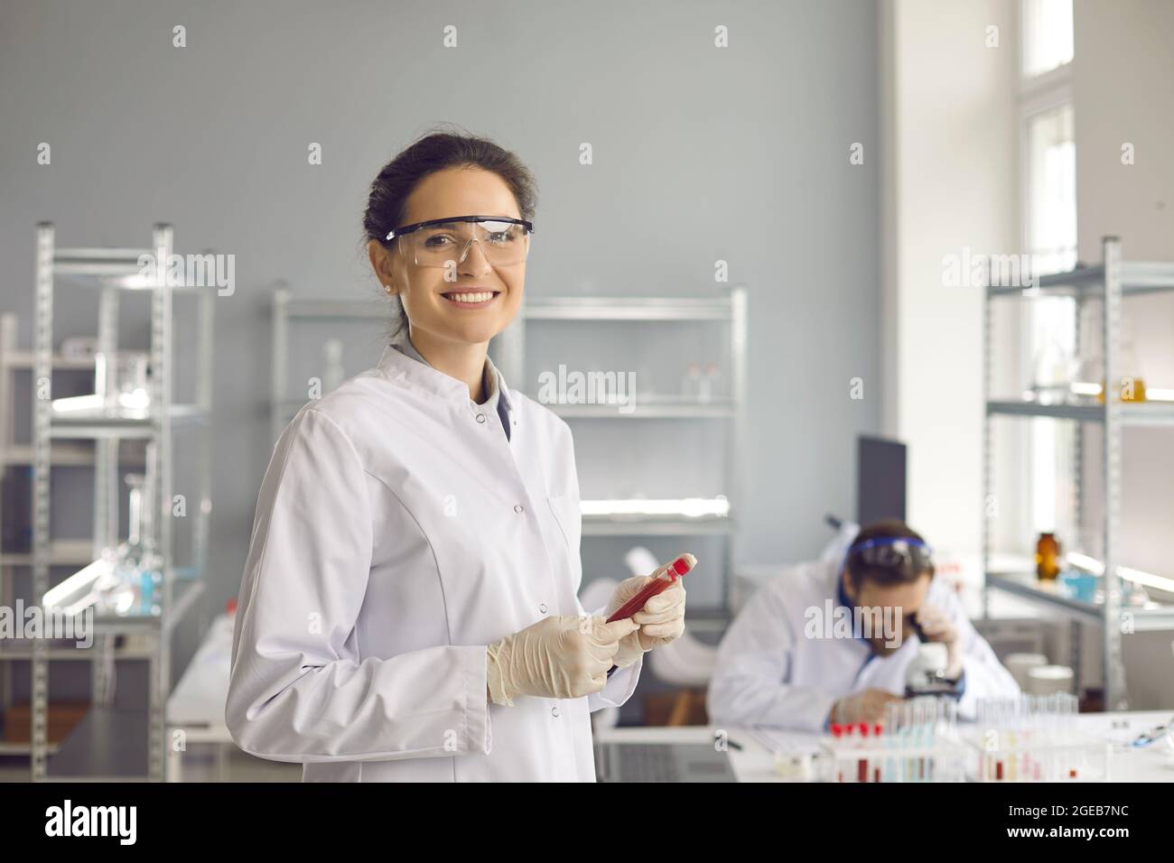 Portrait of happy smiling scientist in lab coat and goggles holding