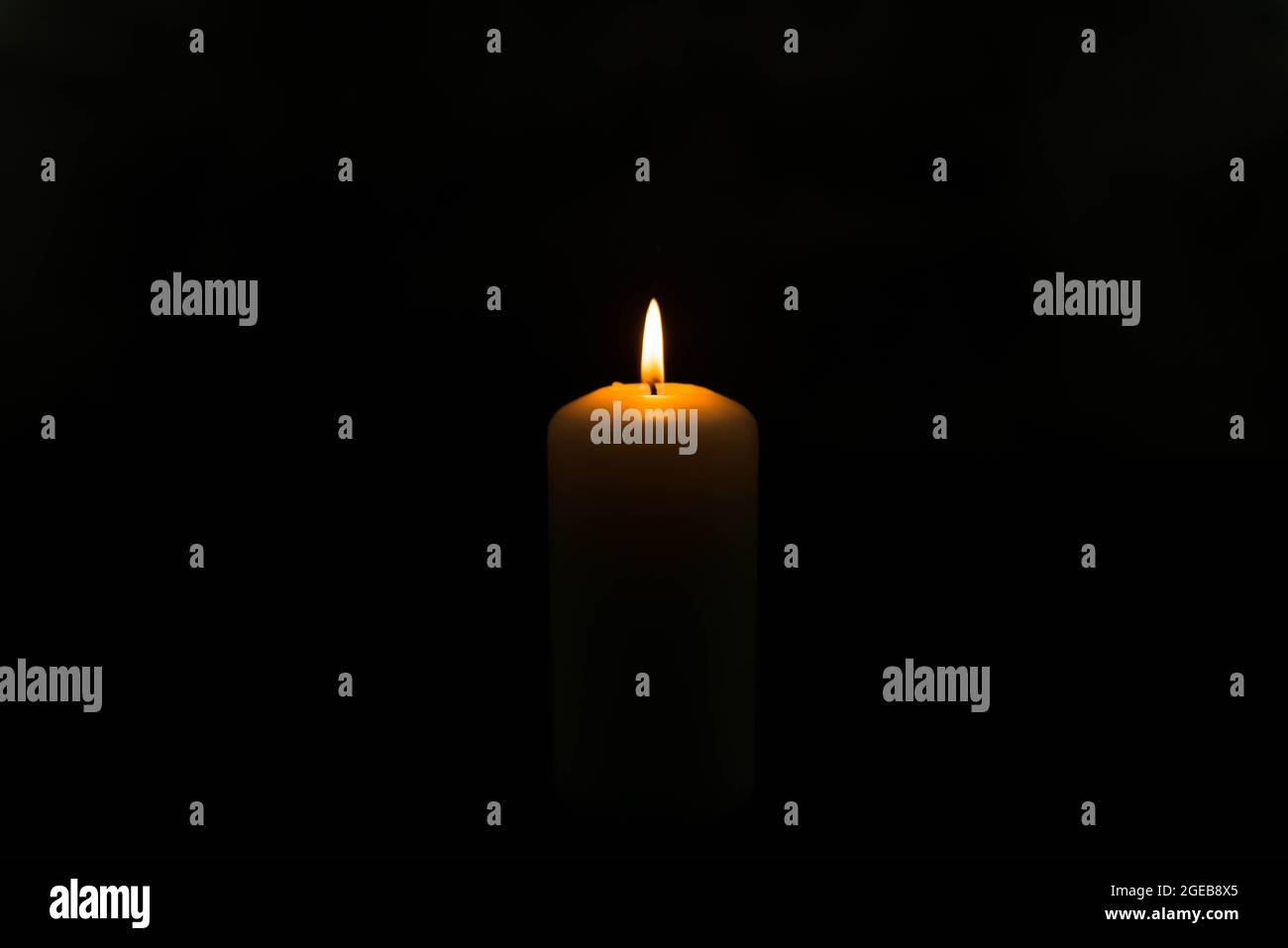 White candle in the dark on a dark background. The candle flame radiates warm yellow light. Stock Photo