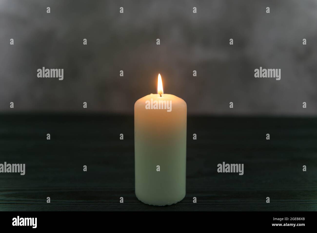 White candle in the dark on a dark background. The candle flame radiates warm yellow light. Stock Photo