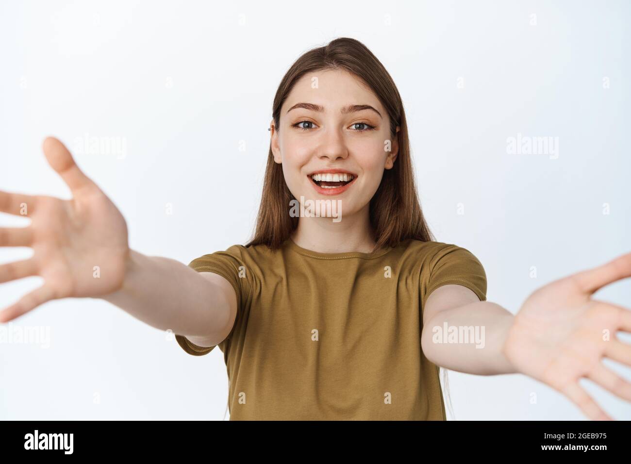 Beautiful girl stretching out hands and smiling, reaching for hug or to  hold something in her arms, standing in t-shirt against white background  Stock Photo - Alamy