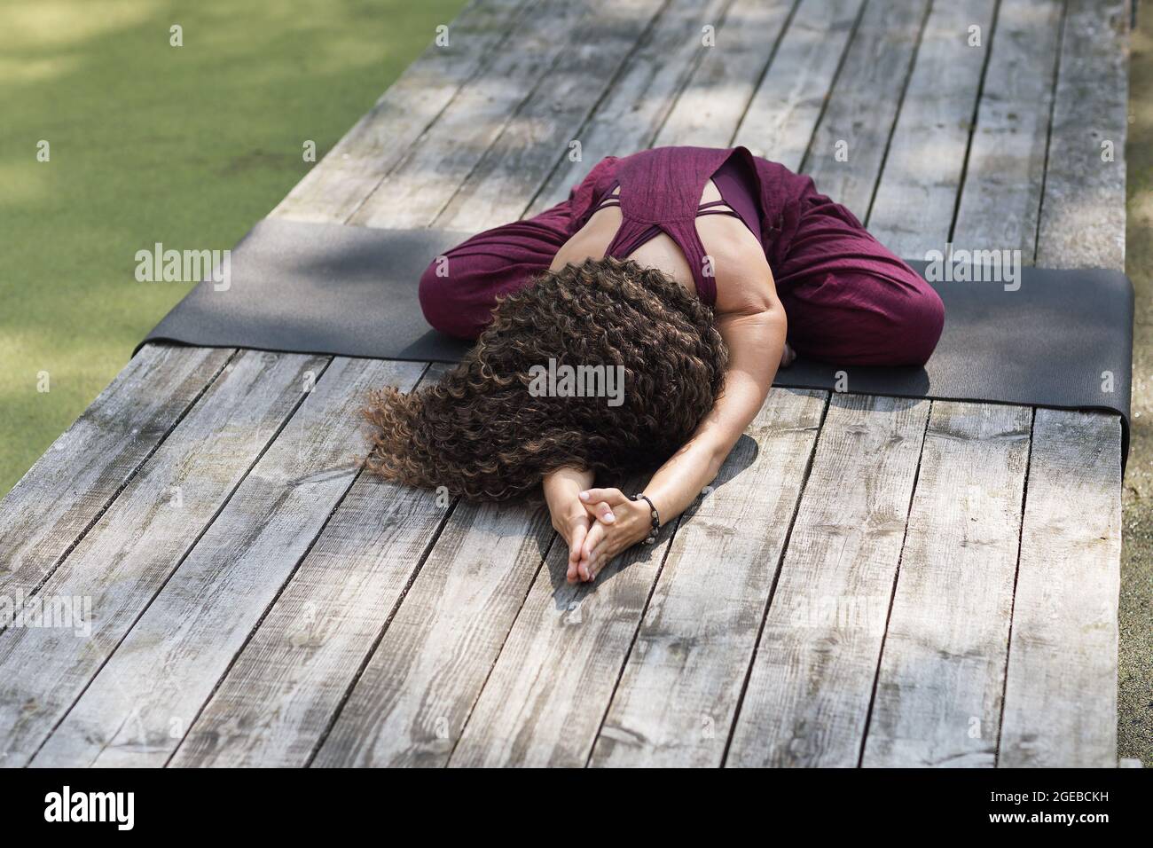 A woman practicing yoga, performs a balasana exercise sitting on a mat in the park, a childs pose Stock Photo