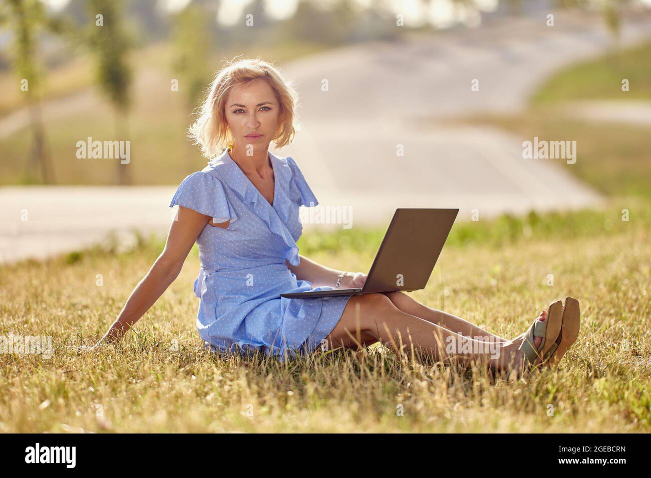 Middle aged woman with laptop sits outdoors in park. Stock Photo