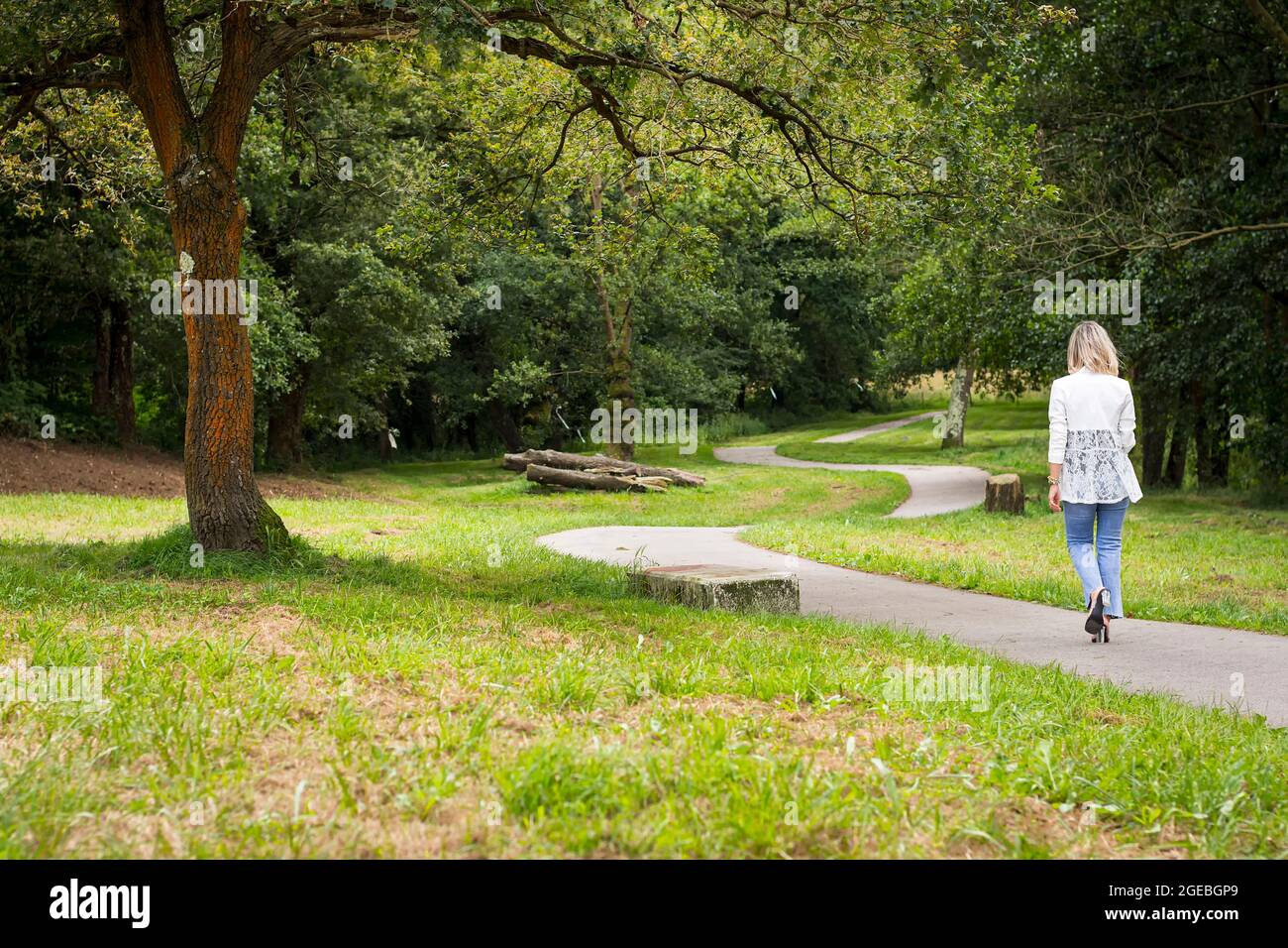 Girl walking with her back to the camera in jeans and a white jacket on a path in a park in Asturias, Spain.Photography taken in horizontal format on Stock Photo