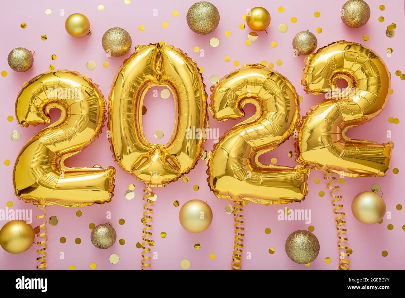 2022 year gold balloons text on ribbons with confetti Christmas gold confetti decor on pink color background. Happy New year 2022 lettering eve Stock Photo