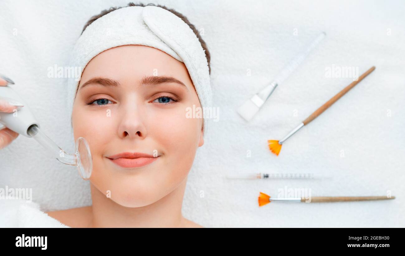 Woman during darsonval cosmetology procedure for skin care lies with beauty injection syringe facial mask brushes cosmetics, tool spa devices on white Stock Photo