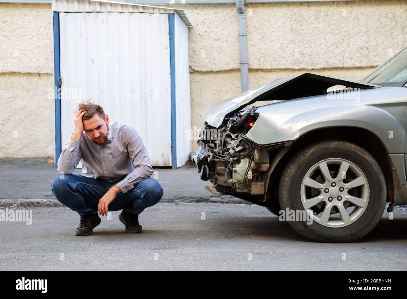 Man holding his head and suffering upset frustrated after car accident. Driver holds head near the wrecked car after car accident on the road Stock Photo