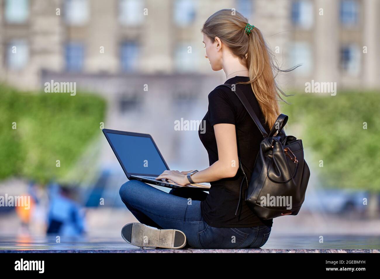 Slender woman in her 30s does remote work on street using laptop. Stock Photo