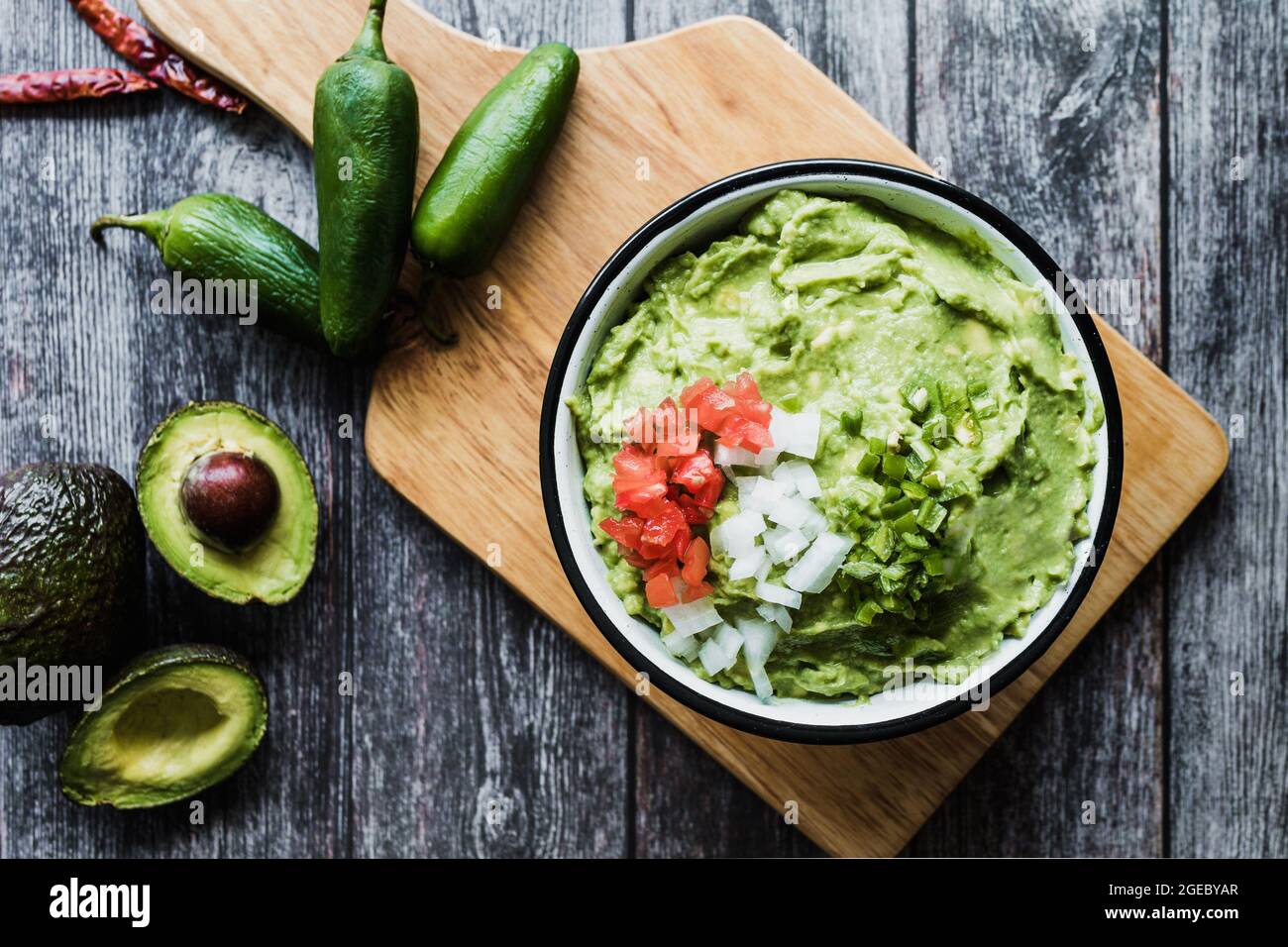 Bowl of Guacamole next to fresh ingredients on a wooden table in Mexico Stock Photo