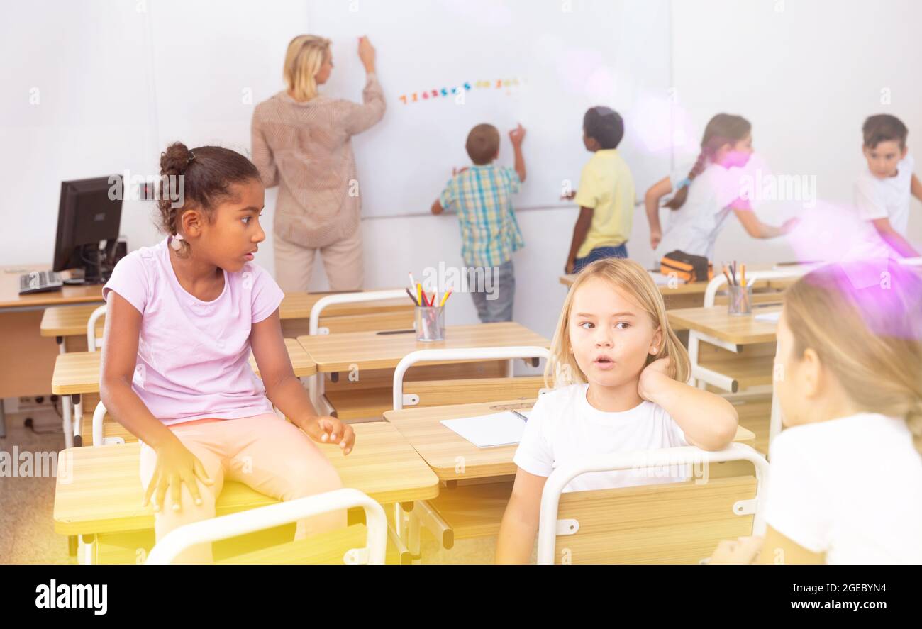 Happy preteen schoolchildren communicating during recess in classroom Stock Photo