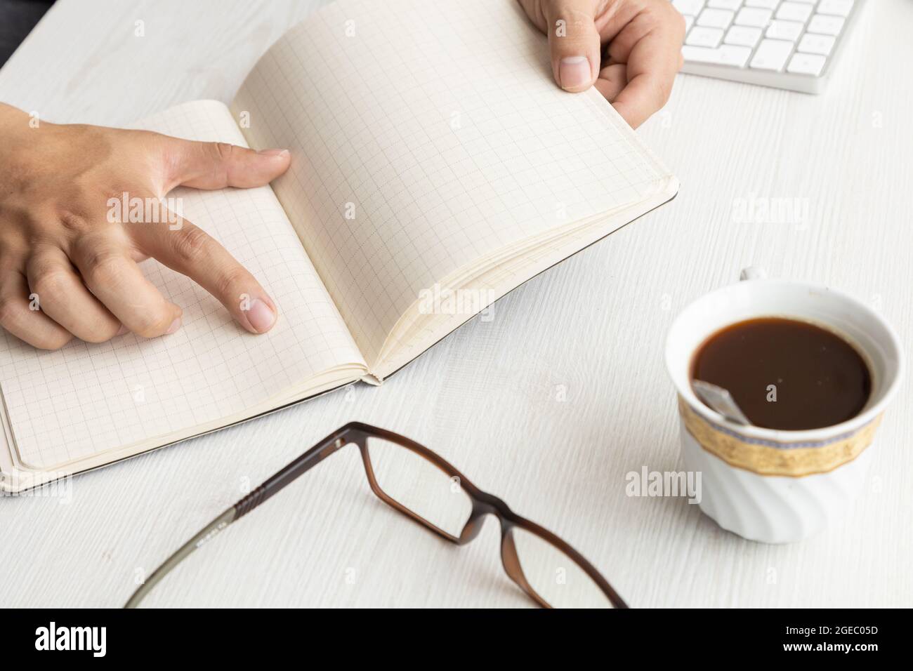 studio with the details of a desk with a person's hands holding and pointing with a notebook with open blank sheets and modern eyeglasses, workplace Stock Photo