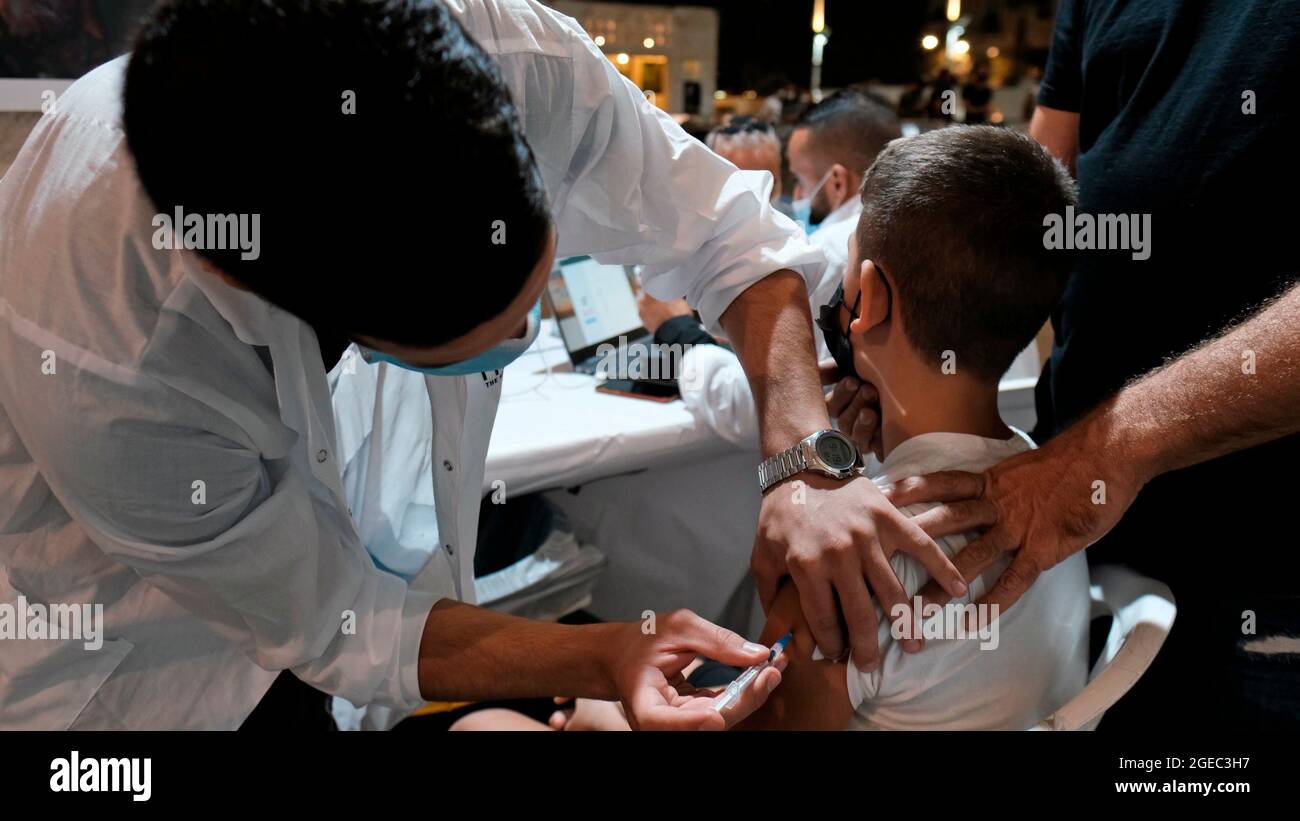 An Israeli health worker administers a dose of the Pfizer-BioNtech COVID-19 vaccine to a young boy at the open night vaccination center in the city hall complex on August 17, 2021 in Jerusalem, Israel. Israel urged more young people to be vaccinated, citing new outbreaks attributed to the more infectious Delta variant. Stock Photo