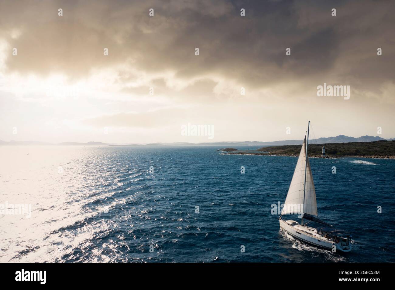 View from above, stunning aerial view of a sailboat sailing on a blue water during a beautiful and dramatic sunset. Costa Smeralda, Sardinia, Italy. Stock Photo