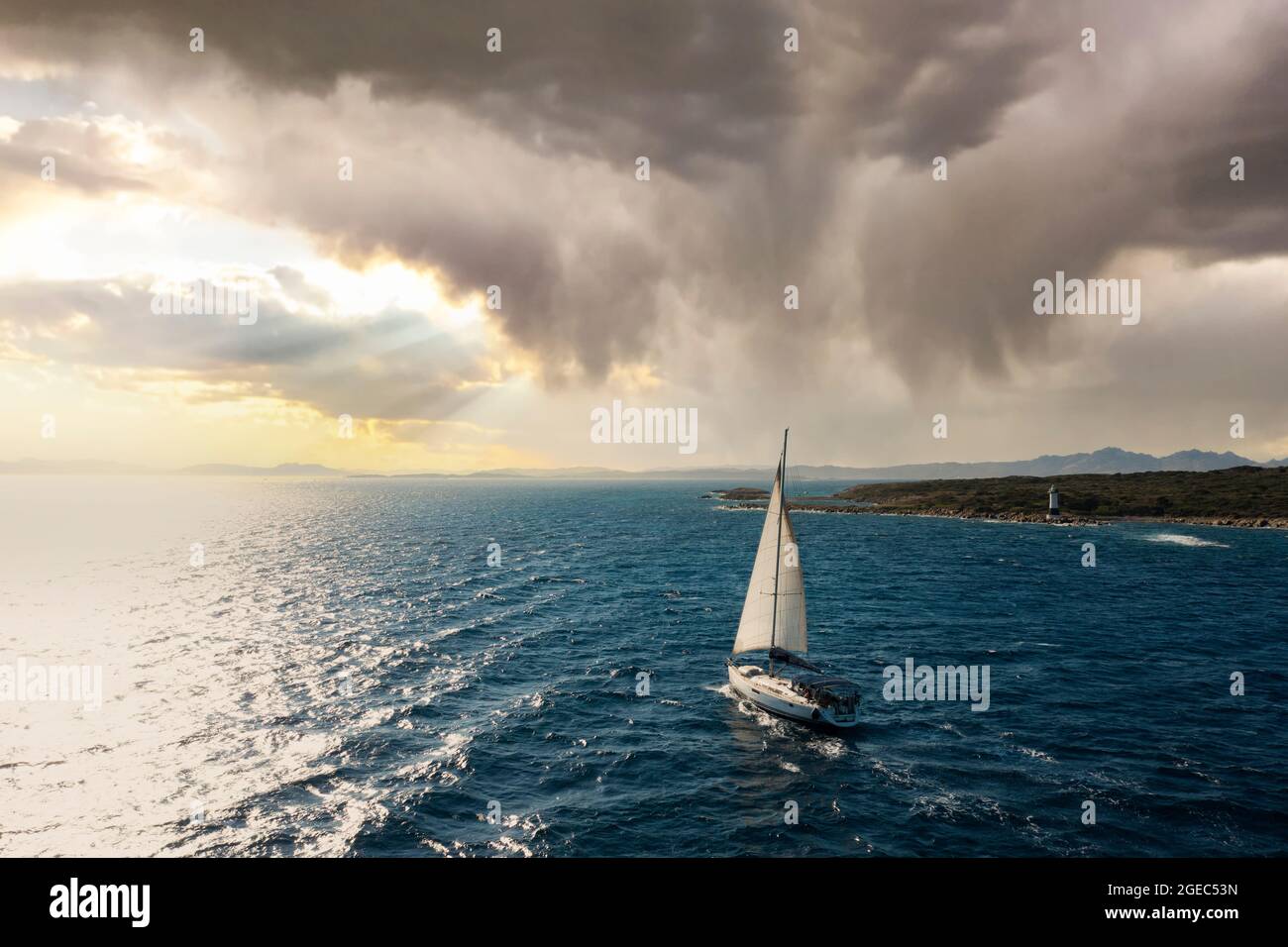 View from above, stunning aerial view of a sailboat sailing on a blue water during a beautiful and dramatic sunset. Costa Smeralda, Sardinia, Italy. Stock Photo