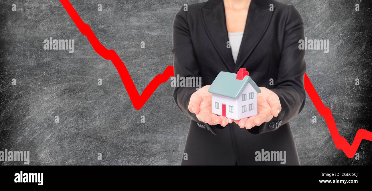 Real estate market crash due to recession economic downturn from coronavirus pandemic crisis. Realtor showing miniature home on red graph blackboard Stock Photo