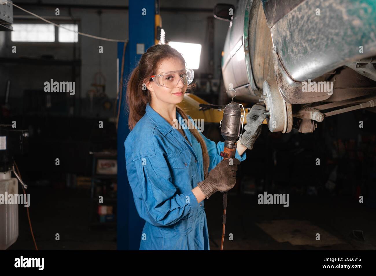 Caucasian woman car mechanic at a real car service station stands and does an inspection of the chassis. Stock Photo