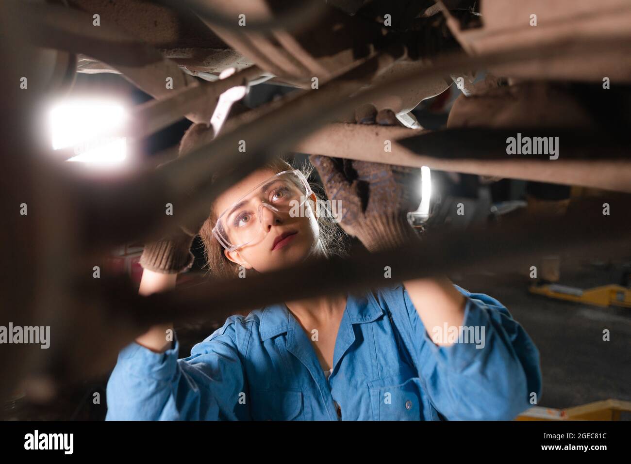 Portrait of a young woman car mechanic makes car repairs. Using a wrench, unscrews the nut. Stock Photo