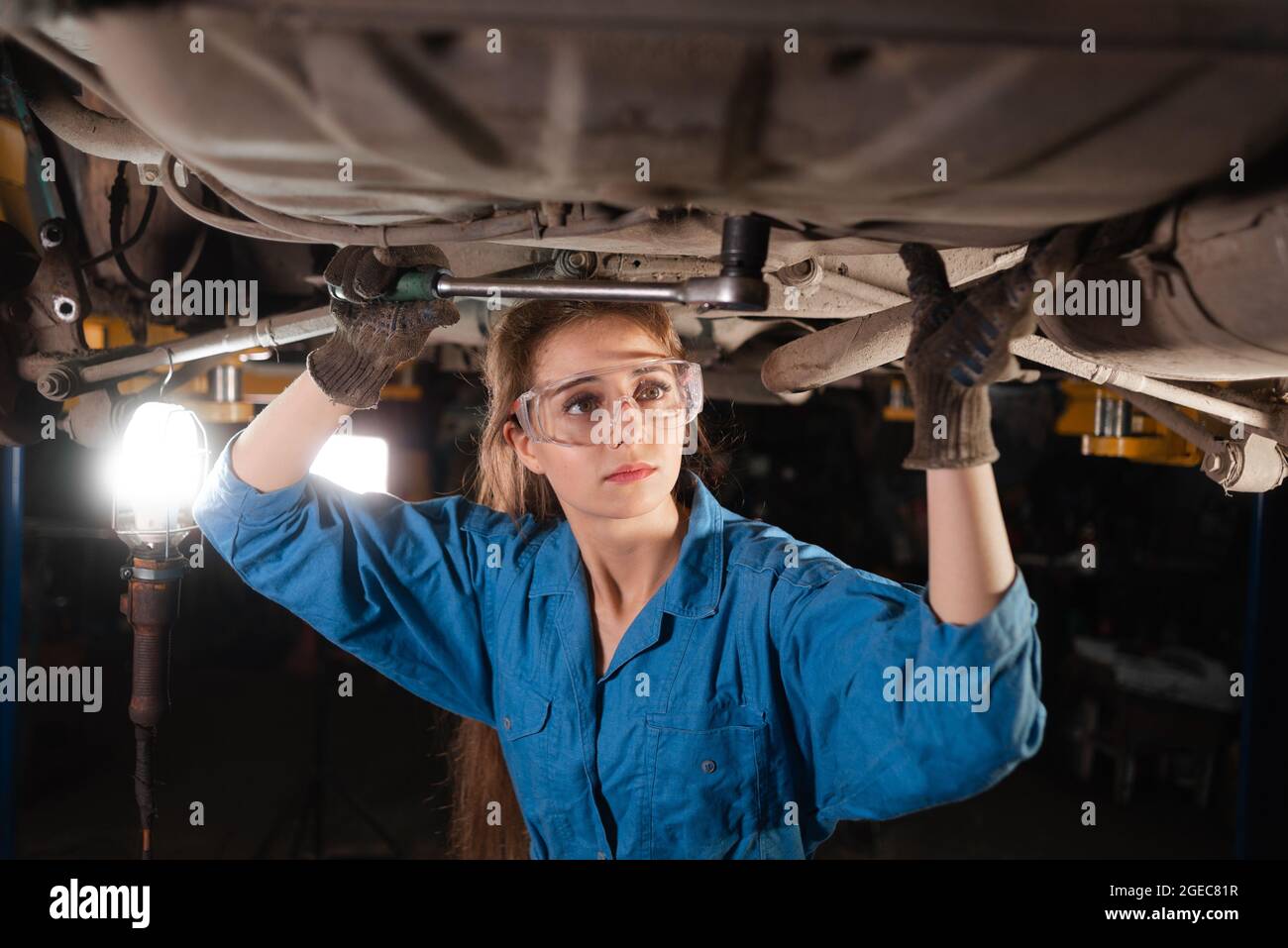 Young beautiful woman car mechanic is dressed in safety glasses and working overalls turns a nut for wrenches. Copy space. Stock Photo