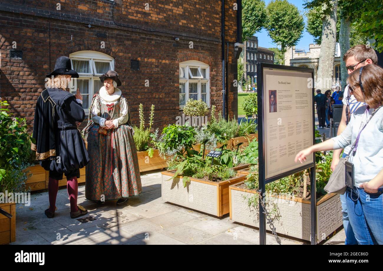 Man and woman in historic Tudor dress in front of the Bloody Tower, Tower of London Complex, with staycation tourist couple reading information board. Stock Photo