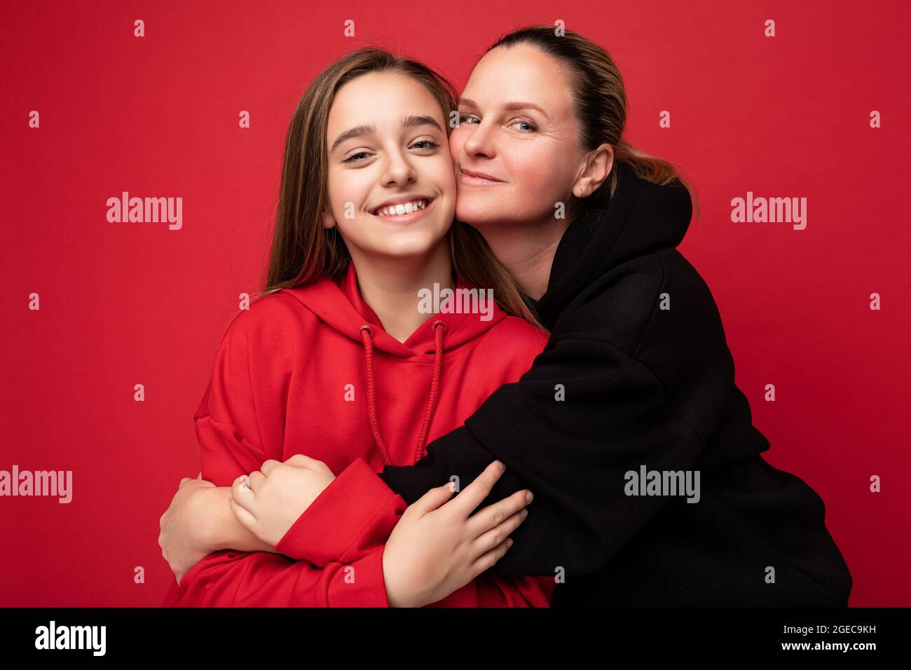 Shot Of Beautiful Happy Smiling Little Daughter Wearing Stylish Red Hoodie And Adult Mother Wearing Trendy Black Hoodie Standing Isolated Over Red Bac Stock Photo Alamy