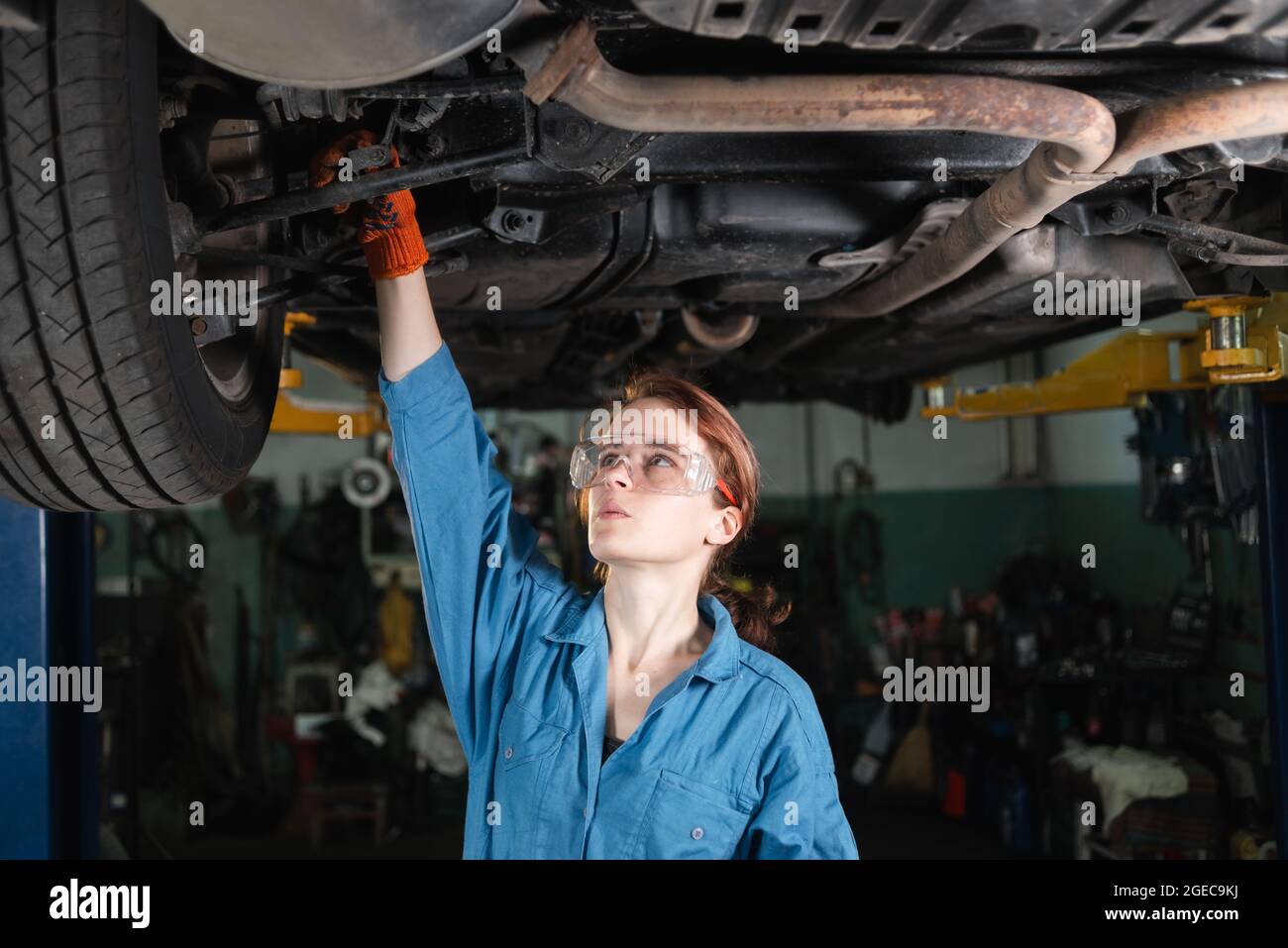 woman car mechanic dressed in glasses and overalls repairs a car. Turns the running gear with a key.4k Stock Photo