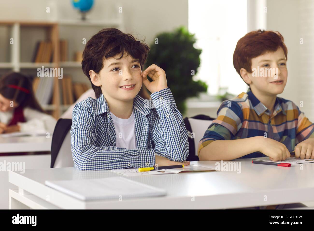 Cute smiling elementary school boy sitting at a desk together with his classmate Stock Photo