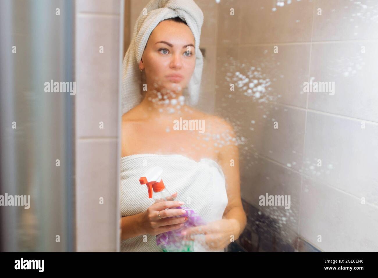 Cleaning in the shower room. A beautiful girl washes the mirror with a rag Stock Photo
